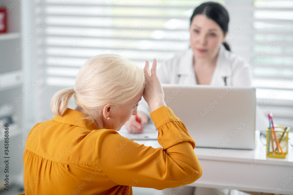 Woman in white coat looking at patient in yellow. Woman in white coat looking at patient in yellow.