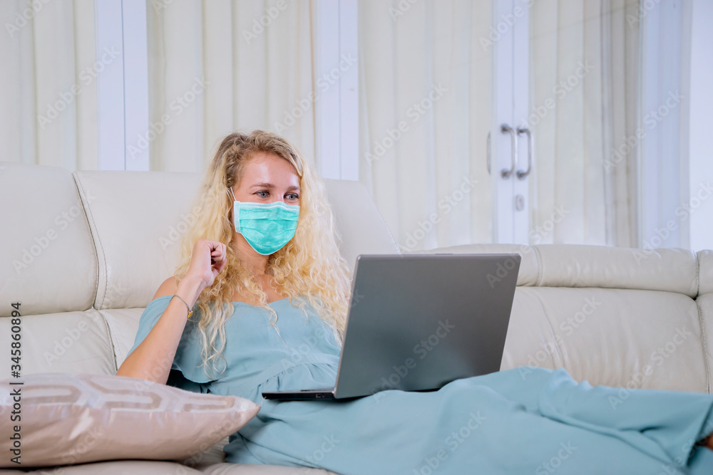 Young woman using laptop at home with face mask Young woman using laptop at home with face mask