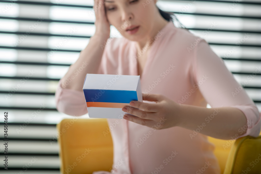 Woman in pink blouse with box of pills in her hand.
