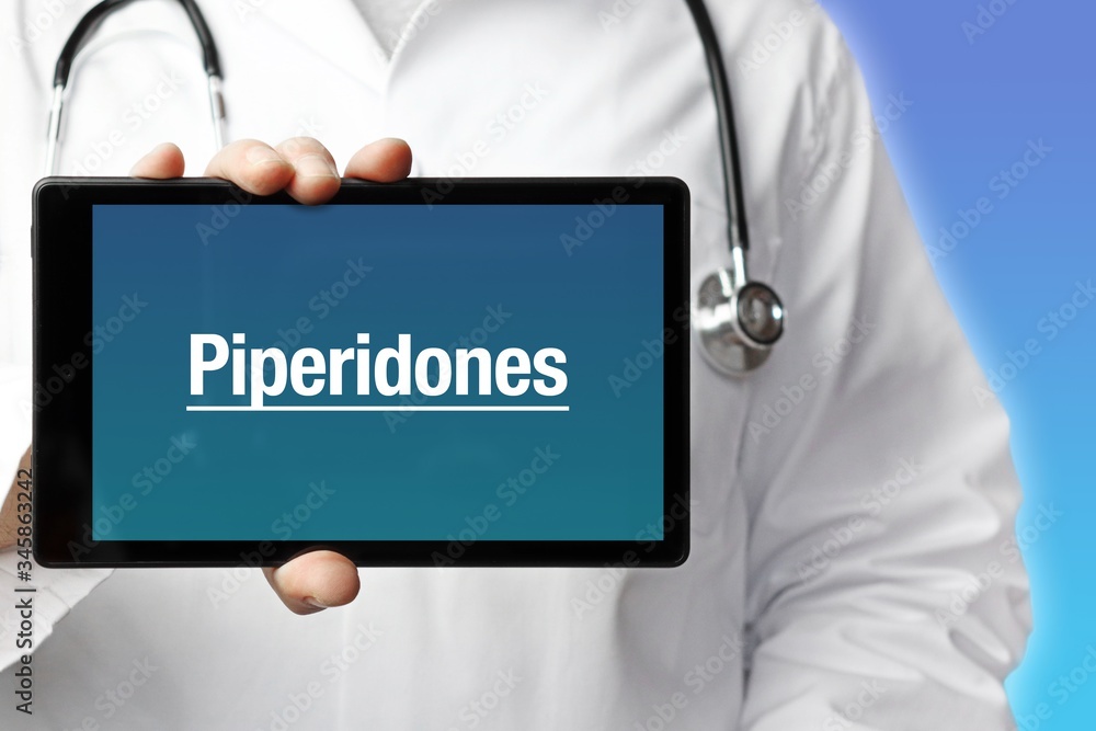 Piperidones. Doctor in smock holds up a tablet computer. The term Piperidones is in the display. Concept of disease, health, medicine