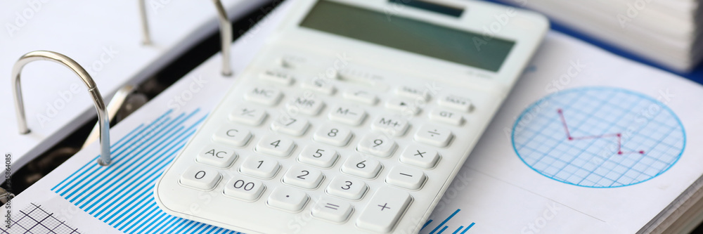 White caculator with business chart lie on the office table background closeup. Financial education concept White caculator with business chart lie on the office table background closeup. Financial education concept