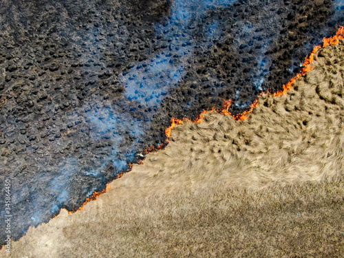 dry grass burns in the field, top view, shooting aerial, spring fire, diagonal fire front, 
