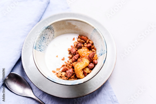 Fototapeta Naklejka Na Ścianę i Meble -  Healthy breakfast yogurt bowl with granola and caramelized bananas and nuts on grey concrete background. Selective focus