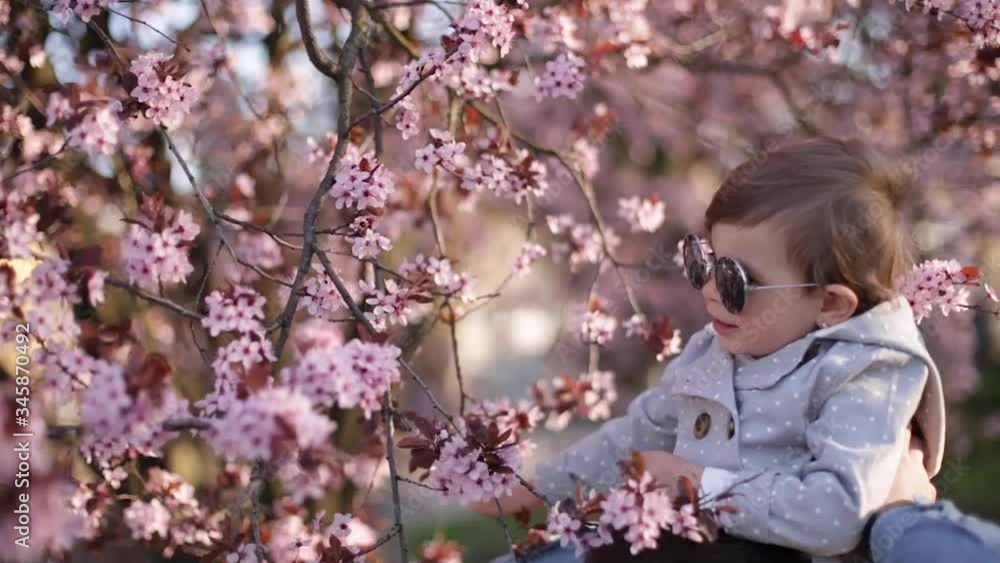 Adorable little daughter sitting on dad's neck and smels pink flowers from flowering tree. Happy family Adorable little daughter sitting on dad's neck and smels pink flowers from flowering tree. Happy family
