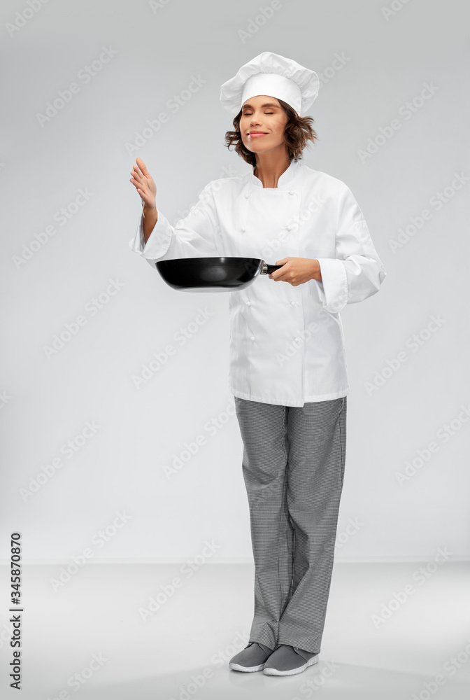 cooking, culinary and people concept - happy smiling female chef in toque with frying pan smelling food flavor over grey background cooking, culinary and people concept - happy smiling female chef in toque with frying pan smelling food flavor over grey background