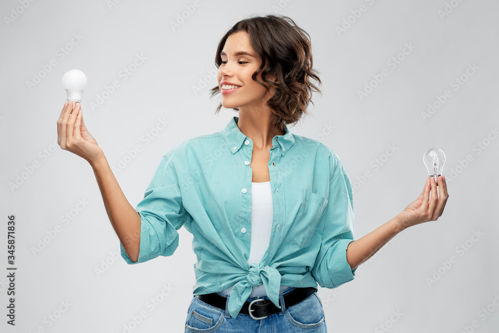 eco living, inspiration and sustainability concept - portrait of happy smiling young woman in turquoise shirt comparing energy saving light bulb with incandescent lamp over grey background eco living, inspiration and sustainability concept - portrait of happy smiling young woman in turquoise shirt comparing energy saving light bulb with incandescent lamp over grey background