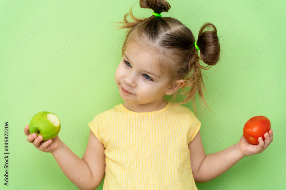 a little girl 3-5 years old in a yellow T-shirt emotionally holds an apple and a tomato in her hands. the problem of lack of fruits and vegetables in baby food a little girl 3-5 years old in a yellow T-shirt emotionally holds an apple and a tomato in her hands. the problem of lack of fruits and vegetables in baby food