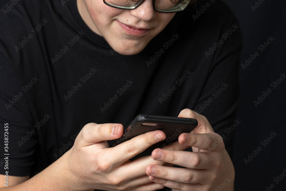 a teenager in glasses looks at a smartphone and smiles. the effect of gadgets on children's vision. 5g and coronavirus a teenager in glasses looks at a smartphone and smiles. the effect of gadgets on children's vision. 5g and coronavirus