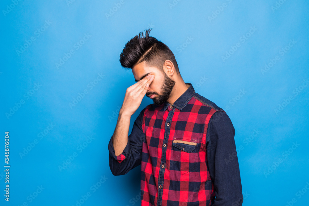 Young indian man wearing elegant shirt and tie standing over isolated blue background with hand on head for pain in head because stress. Suffering migraine. Young indian man wearing elegant shirt and tie standing over isolated blue background with hand on head for pain in head because stress. Suffering migraine.