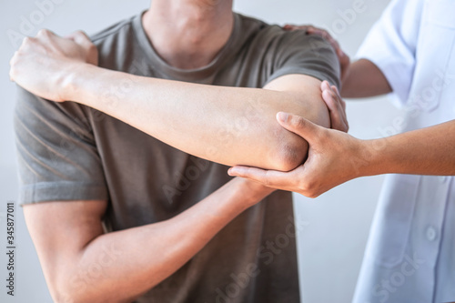 Doctor or Physiotherapist working examining treating injured arm of athlete male patient, stretching and exercise, Doing the Rehabilitation therapy pain in clinic