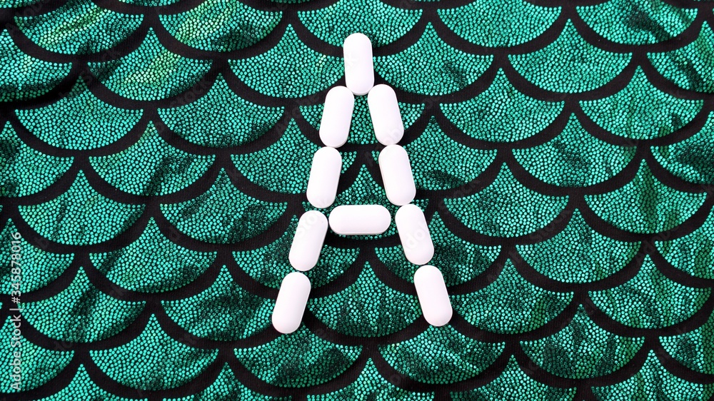 Alphabet made of pills on a green and black background. Vitamins on a background of scales. Abc from drugs. Letter A made from pills. Capital letter A of medicines
