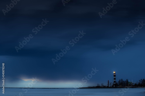 Sea waves of the sea at long exposure. Cloudy sky over the water. Striped lighthouse on the seashore.