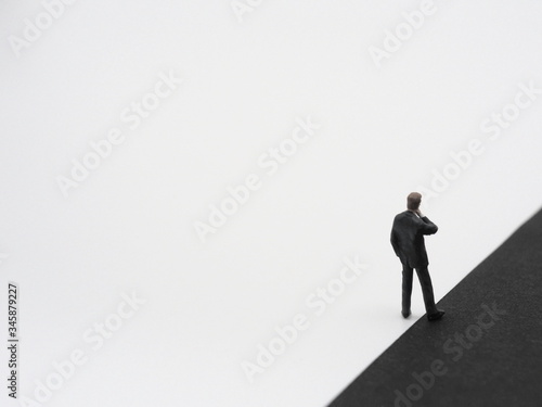 A miniature businessman having one foot in black background. The dark side concept image. © tomatoko