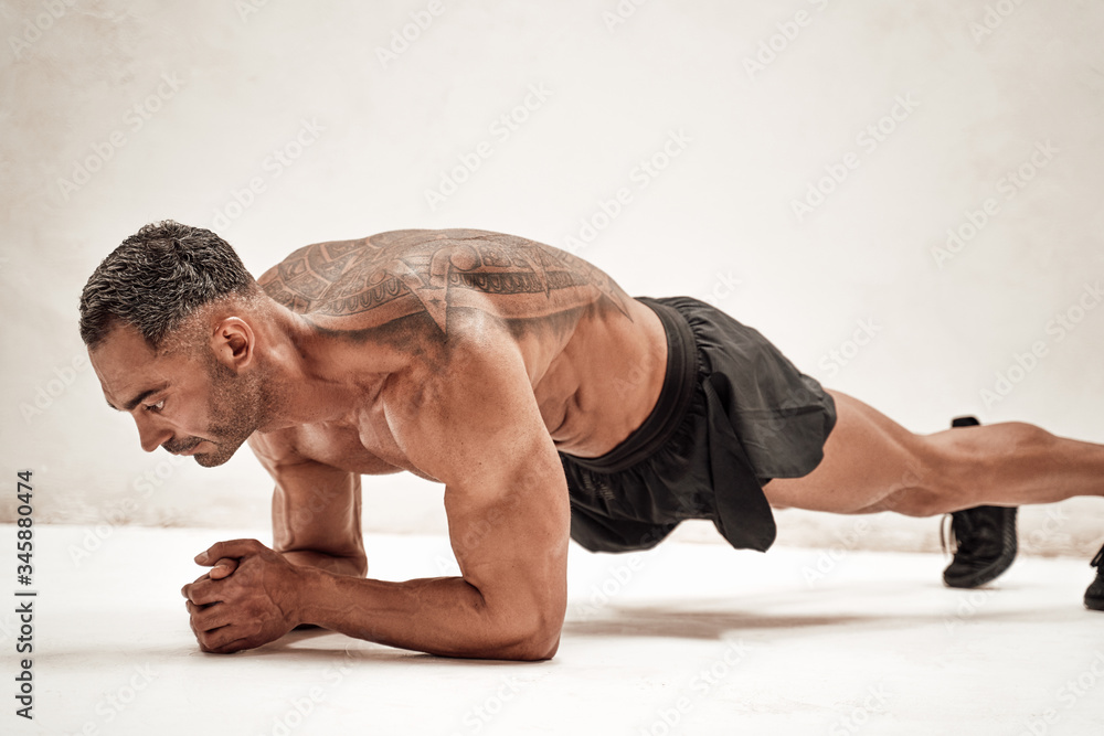 Buffed sportsman posing in a bright studio, while doing an exercise on the floor Buffed sportsman posing in a bright studio, while doing an exercise on the floor