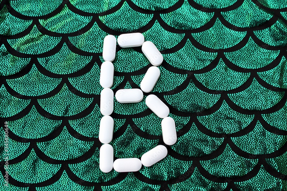 Alphabet made of pills on a green and black background. Vitamins on a background of scales. Abc from drugs. Letter B made from pills. Capital letter B of medicines