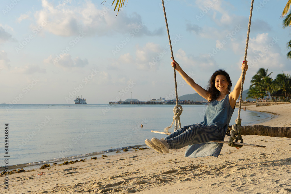 The girl on the beach rides on a swing during sunset. Sunset in the tropics, enjoying nature. Swing tied to a palm tree by the ocean