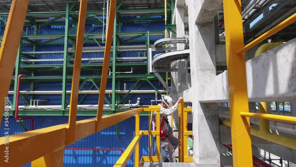 Engineers wear a full body safety harness and climb up the vertical ladder in an industrial factory to check the condition of the equipment. Engineers wear a full body safety harness and climb up the vertical ladder in an industrial factory to check the condition of the equipment.