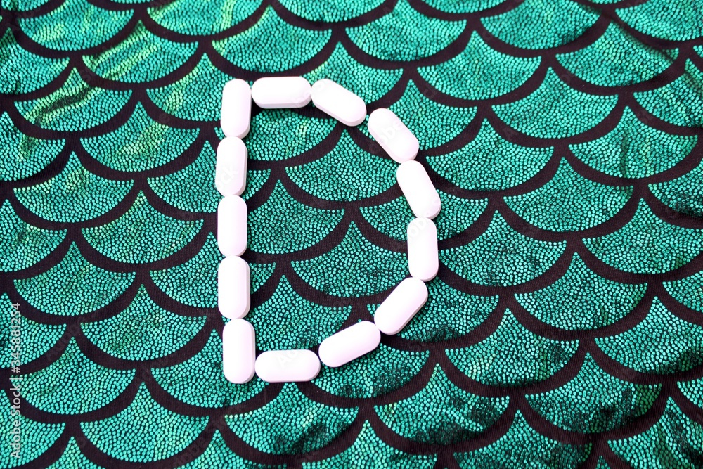 Alphabet made of pills on a green and black background. Vitamins on a background of scales. Abc from drugs. Letter D made from pills. Capital letter D of medicines.