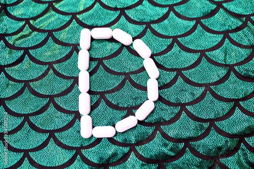 Obraz na płótnie Alphabet made of pills on a green and black background. Vitamins on a background of scales. Abc from drugs. Letter D made from pills. Capital letter D of medicines. w salonie