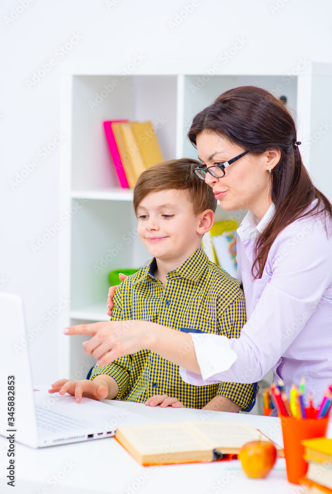 The boy at home with his mom are engaged in school education remotely from home using a laptop. Home Education Concept The boy at home with his mom are engaged in school education remotely from home using a laptop. Home Education Concept