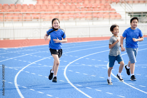 Young Asian boy and girl running on blue track in summer.