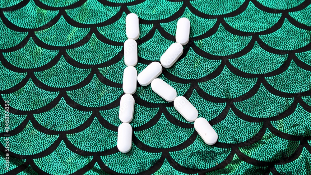 Alphabet made of pills on a green and black background. Vitamins on a background of scales. Abc from drugs. Letter K made from pills. Capital letter K of medicines
