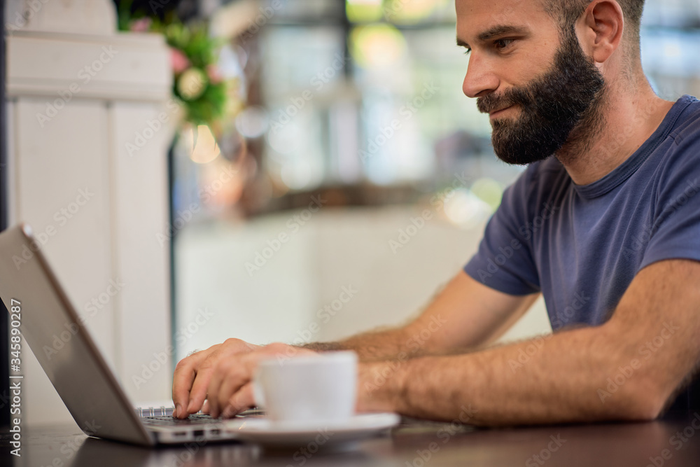Young bearded Caucasian man sitting in restaurant and using laptop. Young bearded Caucasian man sitting in restaurant and using laptop.