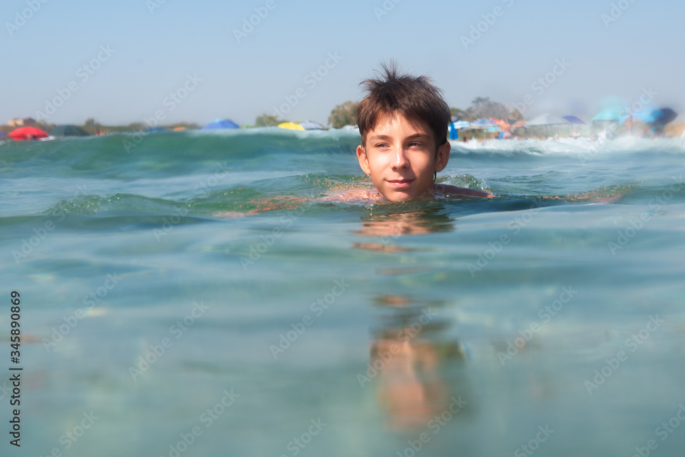Cheerful handsome teen boy swiming in turquoise blue sea water above water surface and underwater. Beach, summer vacation, teenage lifestyle, recreation.