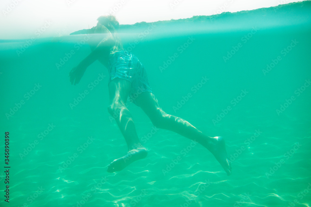 Cheerful handsome teen boy swiming in turquoise blue sea water above water surface and underwater. Beach, summer vacation, teenage lifestyle, recreation.