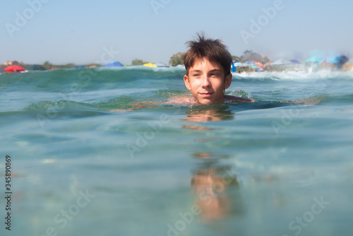 Cheerful handsome teen boy swiming in turquoise blue sea water above water surface and underwater. Beach, summer vacation, teenage lifestyle, recreation.