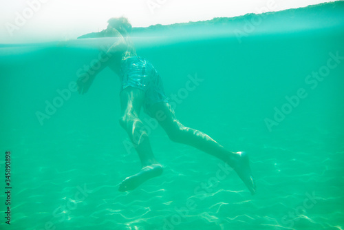 Cheerful handsome teen boy swiming in turquoise blue sea water above water surface and underwater. Beach  summer vacation  teenage lifestyle  recreation.