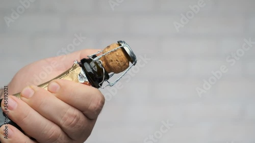 man opens bottle of champagne on light background. cork flies out of bottle of sparkling wine when male hand opens it closeup. photo