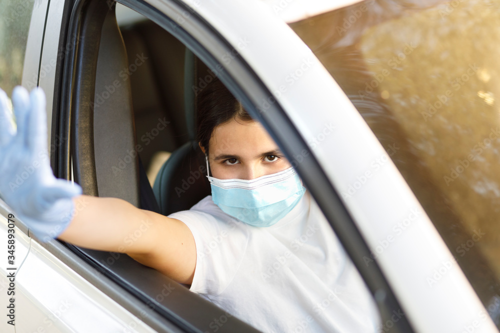 bambina con i capelli neri indossa una mascherina facciale e guanti in lattice per proteggersi fa stop con la mano dall'abitacolo di un automobile bambina con i capelli neri indossa una mascherina facciale e guanti in lattice per proteggersi fa stop con la mano dall'abitacolo di un automobile