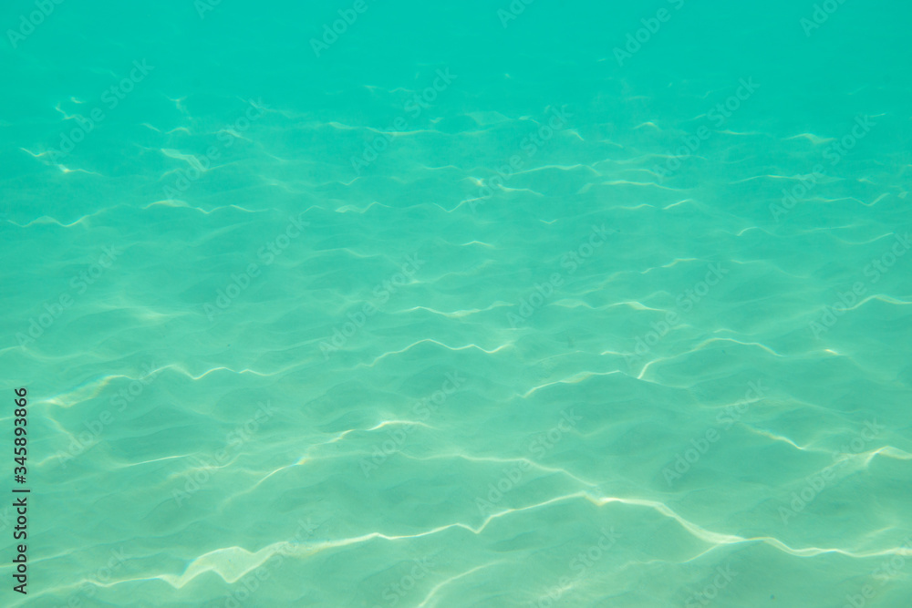 Underwater. Sun glare at the bottom of the sea. Waves underwater and rays of sunlight shining through. Deep turquoise blue sea. Ocean. Transparent water and light at sand.