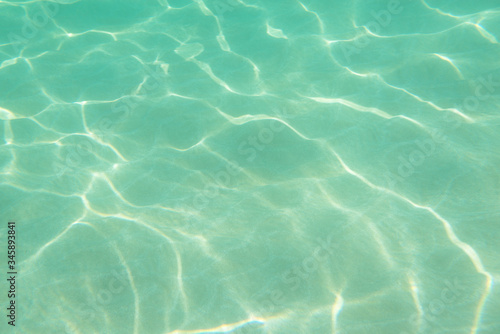 Underwater. Sun glare at the bottom of the sea. Waves underwater and rays of sunlight shining through. Deep turquoise blue sea. Ocean. Transparent water and light at sand.