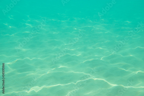 Underwater. Sun glare at the bottom of the sea. Waves underwater and rays of sunlight shining through. Deep turquoise blue sea. Ocean. Transparent water and light at sand.
