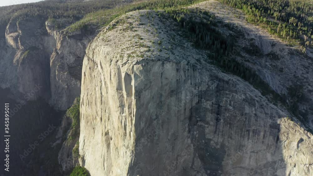 Aerial top-down shot of a densely forested valley at the foot of the massive granite rock El Capitan in Yosemite National Park. Vertical smooth walls of the mountain rise high over the valley. 4K Aerial top-down shot of a densely forested valley at the foot of the massive granite rock El Capitan in Yosemite National Park. Vertical smooth walls of the mountain rise high over the valley. 4K