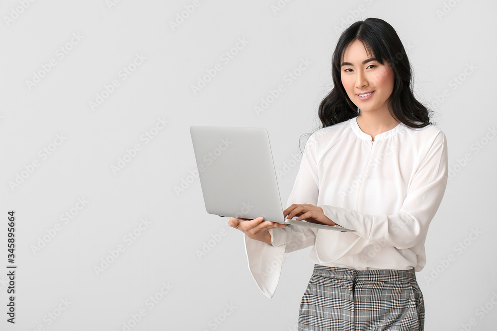 Beautiful Asian secretary with laptop on light background Beautiful Asian secretary with laptop on light background