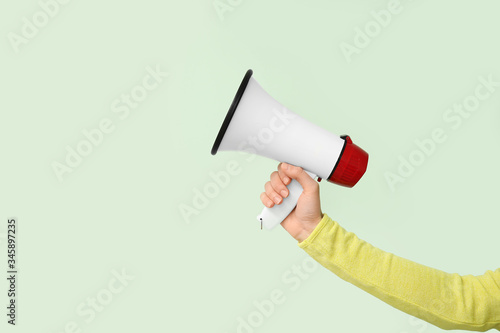 Female hand with megaphone on color background