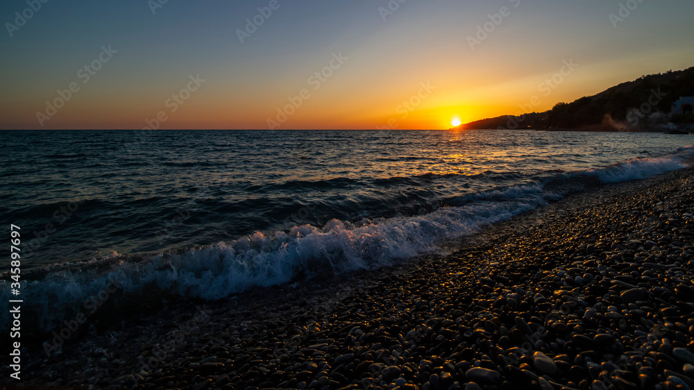 Obraz premium Sunset at sea. Pebble beach, waves