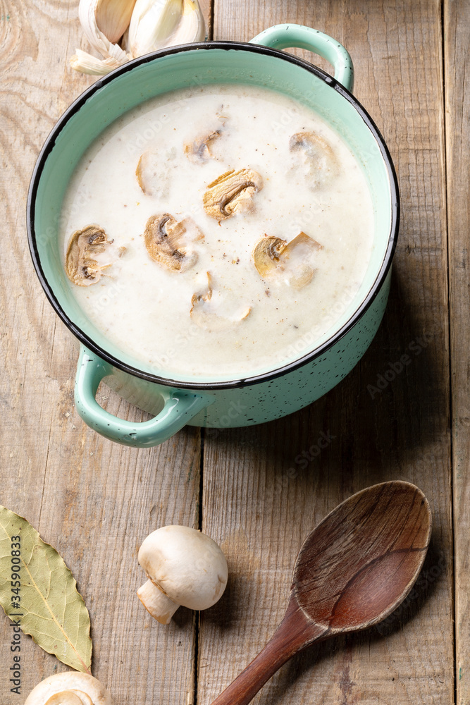 Turquoise ceramic pan with mushroom cream soup, fresh champignons, spoon, garlic and bay leafs on wooden background. Turquoise ceramic pan with mushroom cream soup, fresh champignons, spoon, garlic and bay leafs on wooden background.
