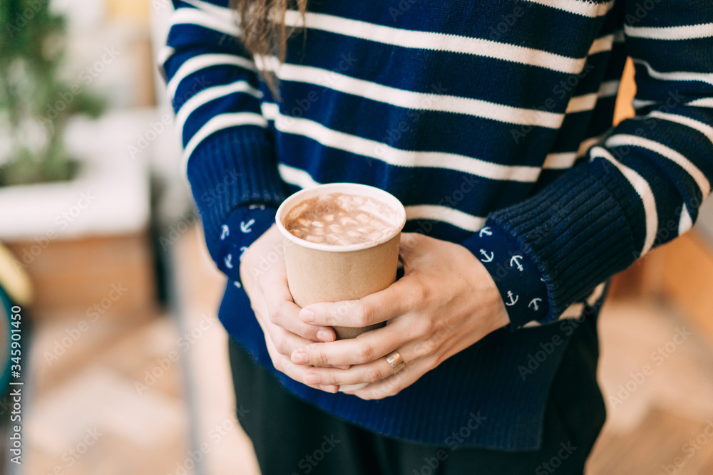 Closeup girl holding a mug with cocoa and marshmallows. A delicious drink in a disposable cup that you can take away Closeup girl holding a mug with cocoa and marshmallows. A delicious drink in a disposable cup that you can take away