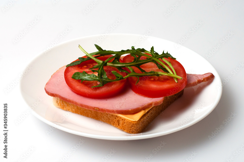 Sandwich of balyk, cheese, bread, tomatoes and arugula on a white plate on a plate view from the side