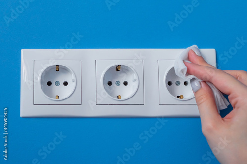 Woman cleaning electrical european outlet, socket with disinfectant wet wipe - close up view. Disinfection, protection, prevention, housework, COVID-19, coronavirus safety and sanitation concept