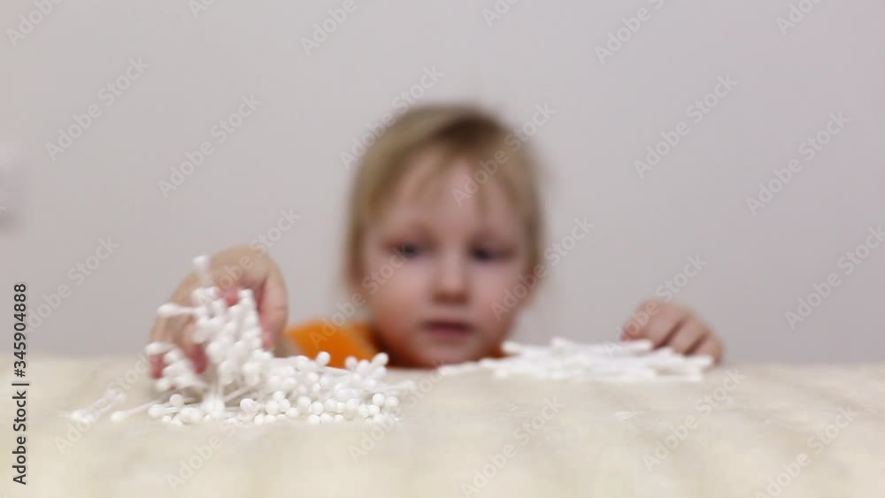 Little beautiful girl takes cotton buds from a table for cleaning ears and skin care, copy space, cotton Little beautiful girl takes cotton buds from a table for cleaning ears and skin care, copy space, cotton