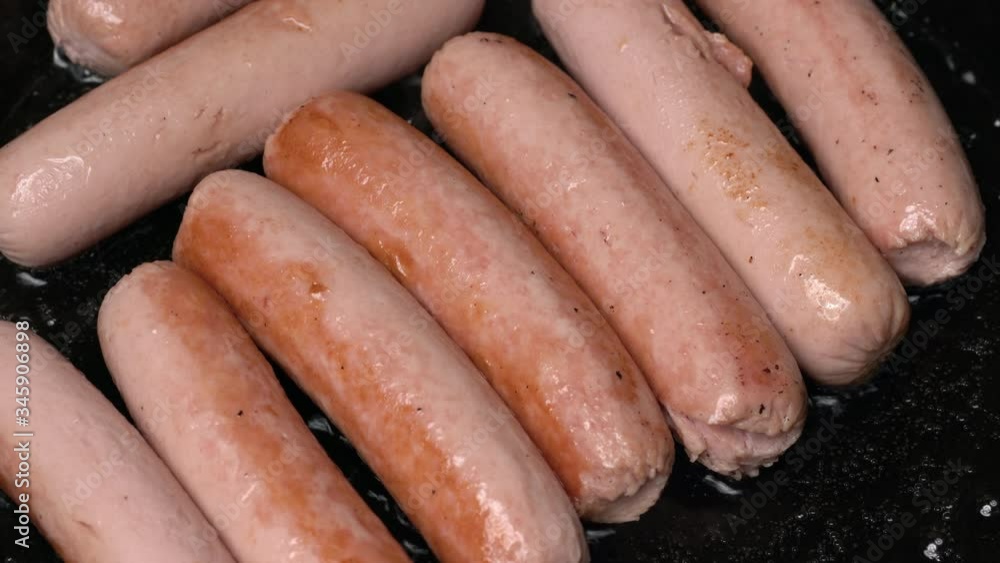 Close up of meat sausages fried in black pan with oil. Close-up view of cooking of delicious, high-calorie non-vegetarian junk food with large content of cholesterol.