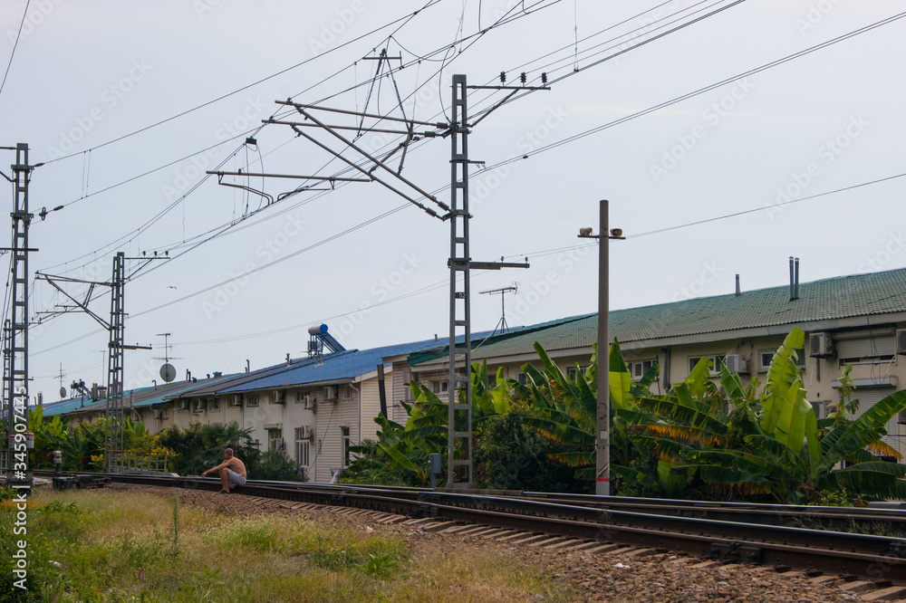 At a crossroads - a man sits with a bare torso and shorts on the railway tracks and smokes.