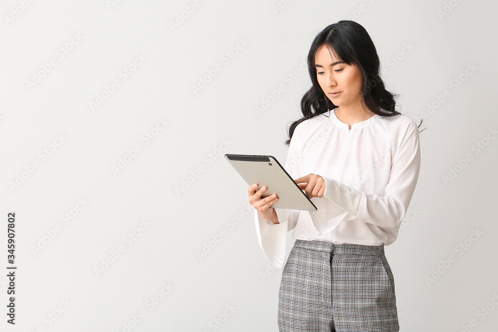 Beautiful Asian secretary with tablet computer on light background Beautiful Asian secretary with tablet computer on light background