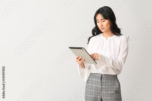 Beautiful Asian secretary with tablet computer on light background