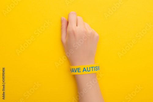 top view of woman hand in bracelet with I have autism inscription on yellow